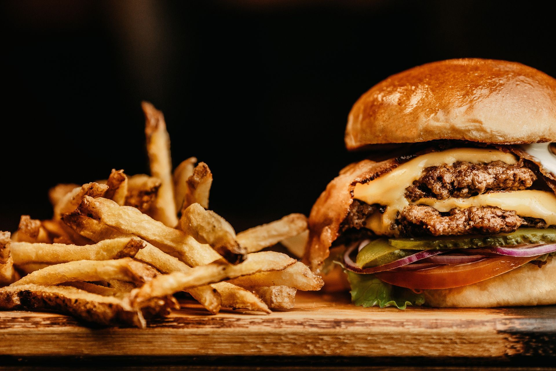 Burger with fries on a wooden board. Double patty, cheese, and toppings visible.
