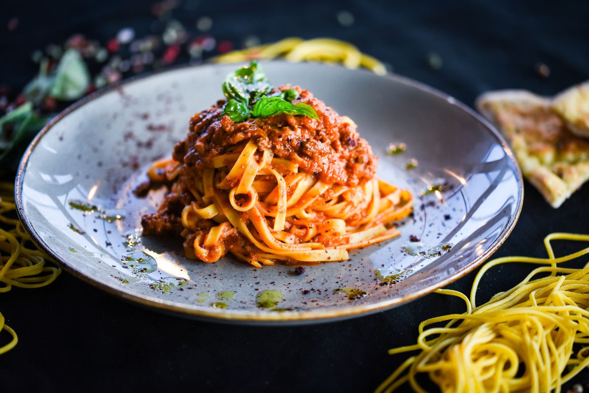 Plated spaghetti with rich meat sauce and herbs on a gray dish, with loose pasta strands around it