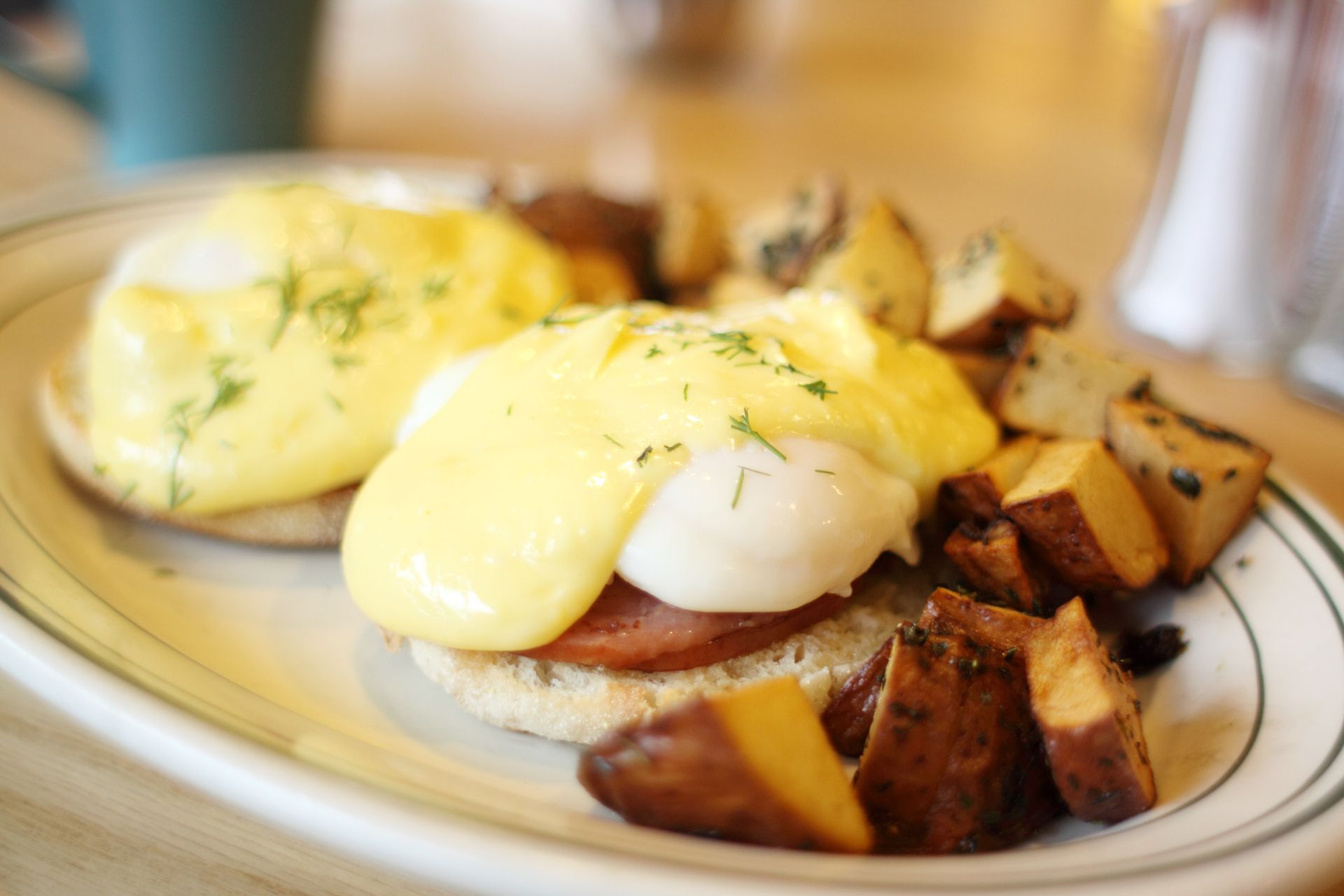Eggs Benedict with hollandaise sauce, Canadian bacon, and potato cubes on a plate.