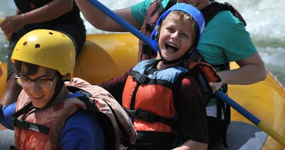 People on a raft in whitewater rapids, smiling, wearing helmets and life vests.
