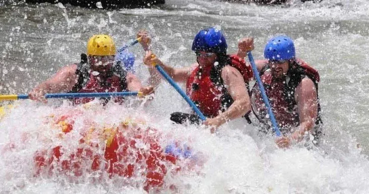 People white water rafting through splashing, churning water.