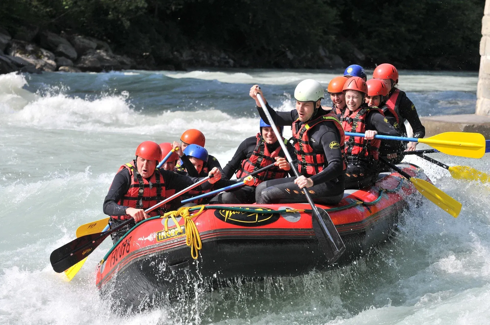 Rafters in helmets and life vests paddle a red raft through white water rapids.