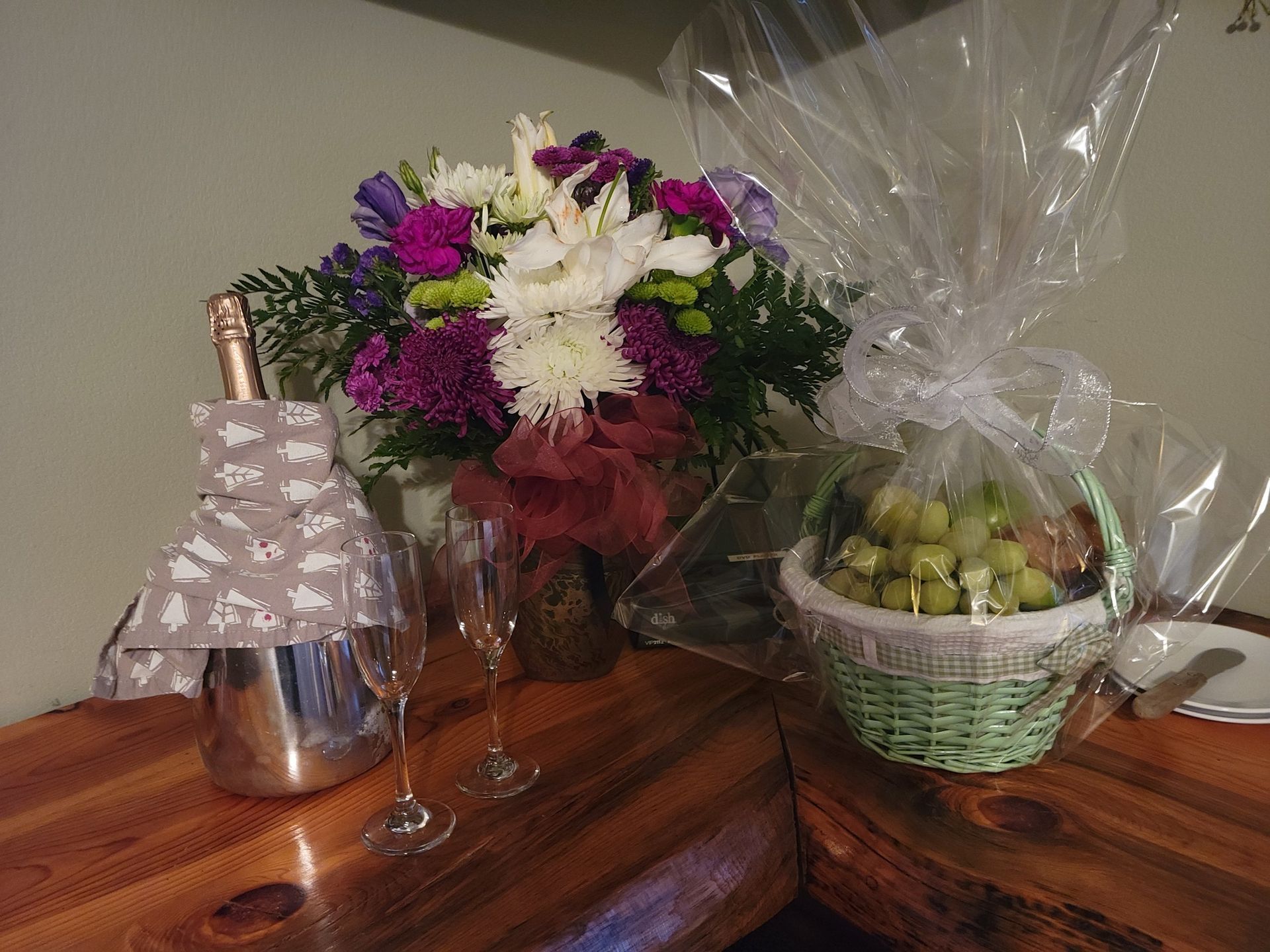 Champagne bottle, flowers, grapes, and glasses on a wooden surface, festive setting.