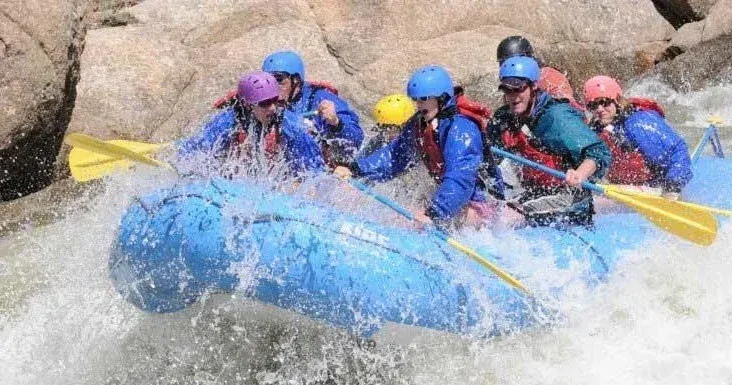 People rafting down a river, paddling through splashing white water.