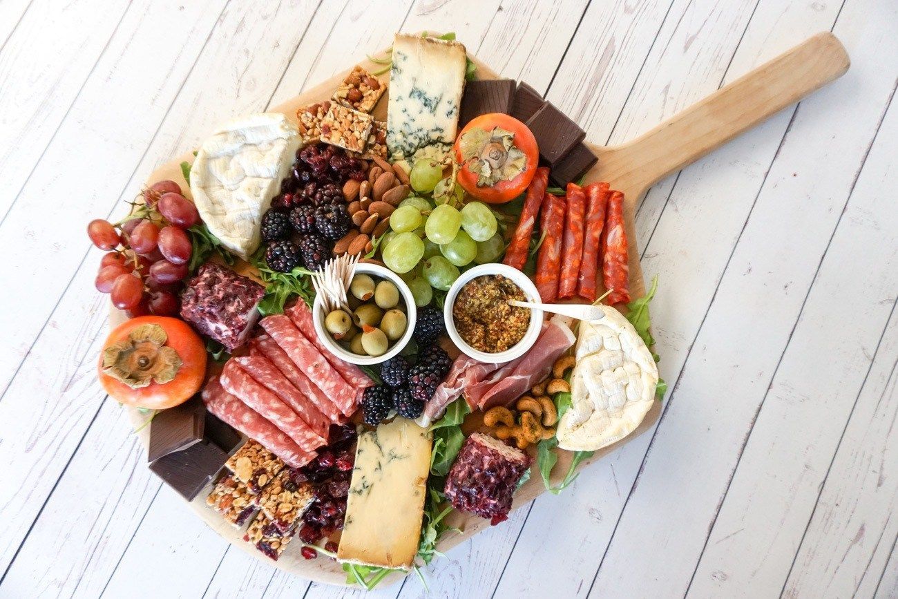Charcuterie board on a wooden paddle, assorted cheeses, meats, fruits, nuts, and olives.