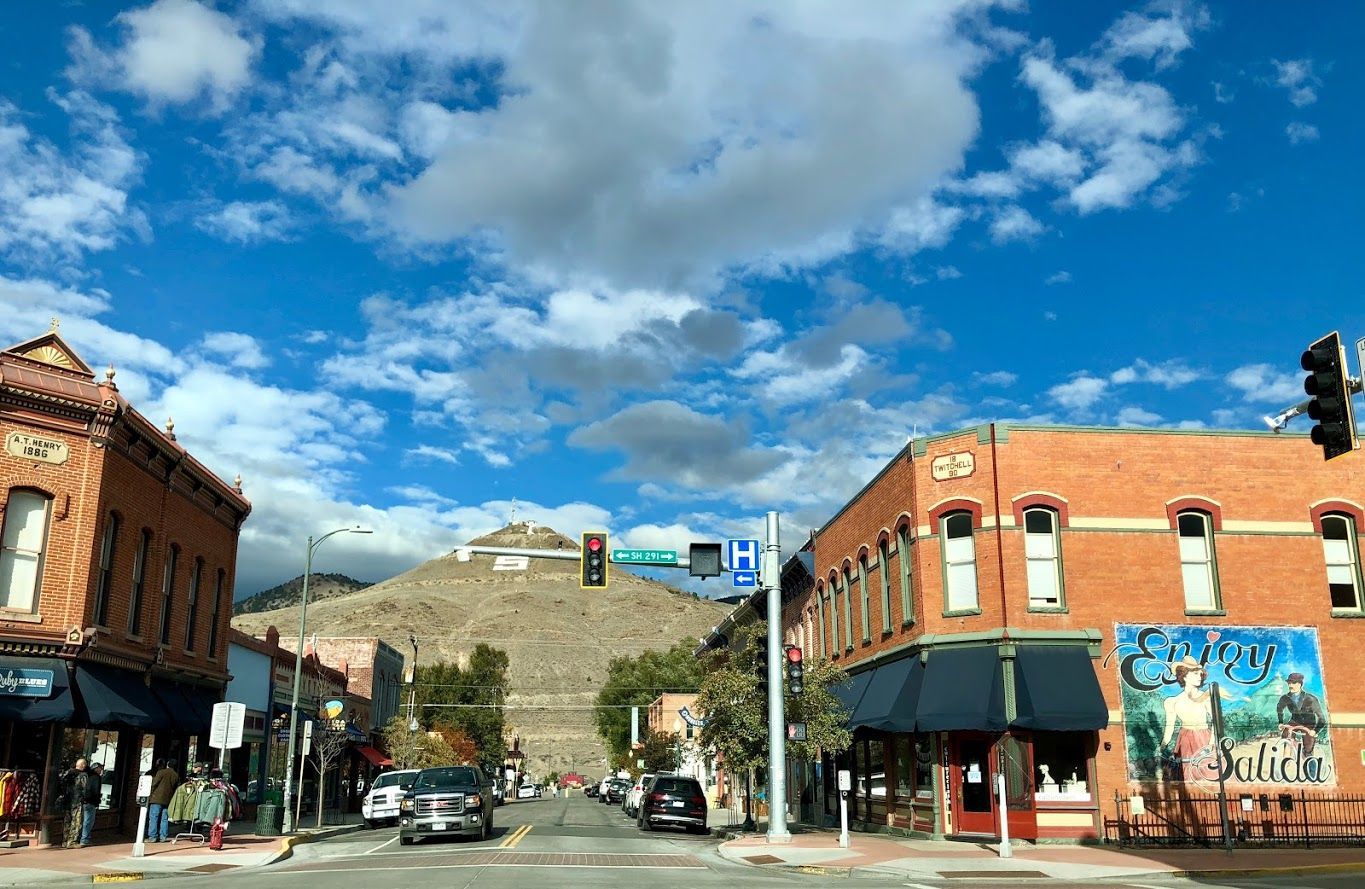 Street scene with brick buildings, blue sky, and a mountain in the background.
