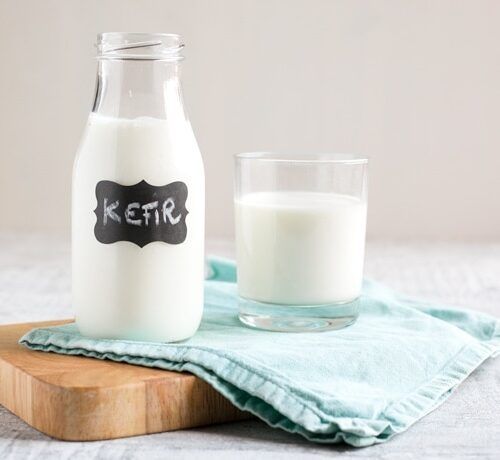 Bottle and glass of kefir on a wooden board and blue cloth. Bottle has a 