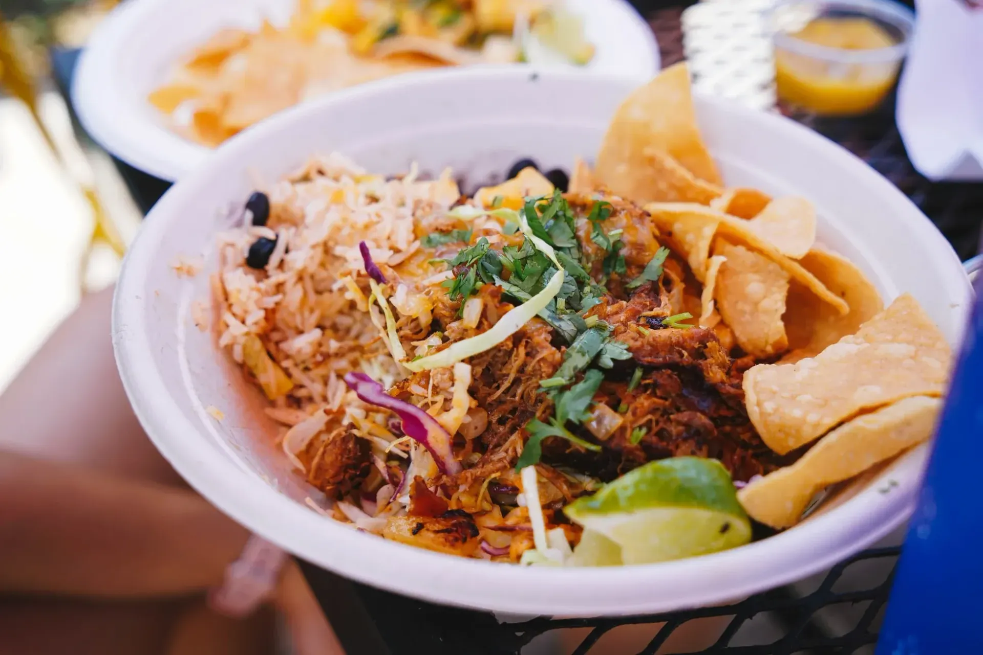 A bowl of food with rice, meat, chips, and garnishes.
