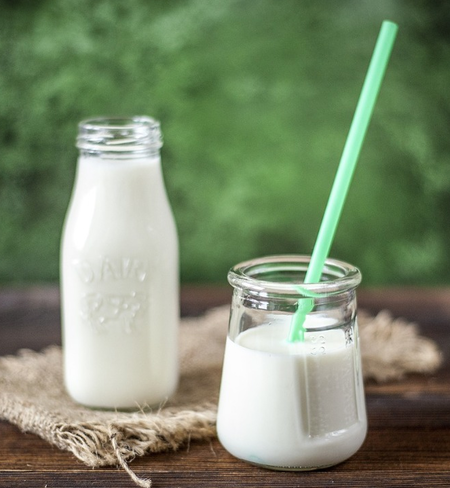 A bottle and small glass of white milk on a wooden surface with a green straw.