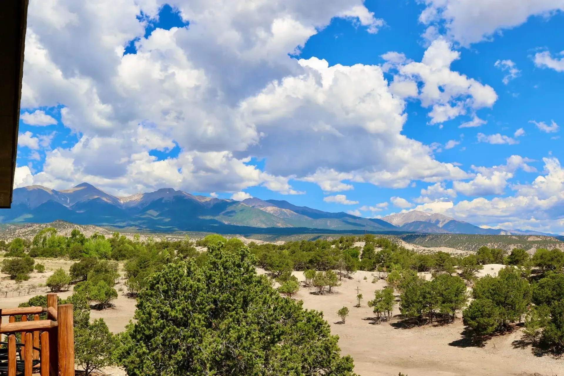 Mountains, blue sky with puffy clouds, desert landscape, green trees.