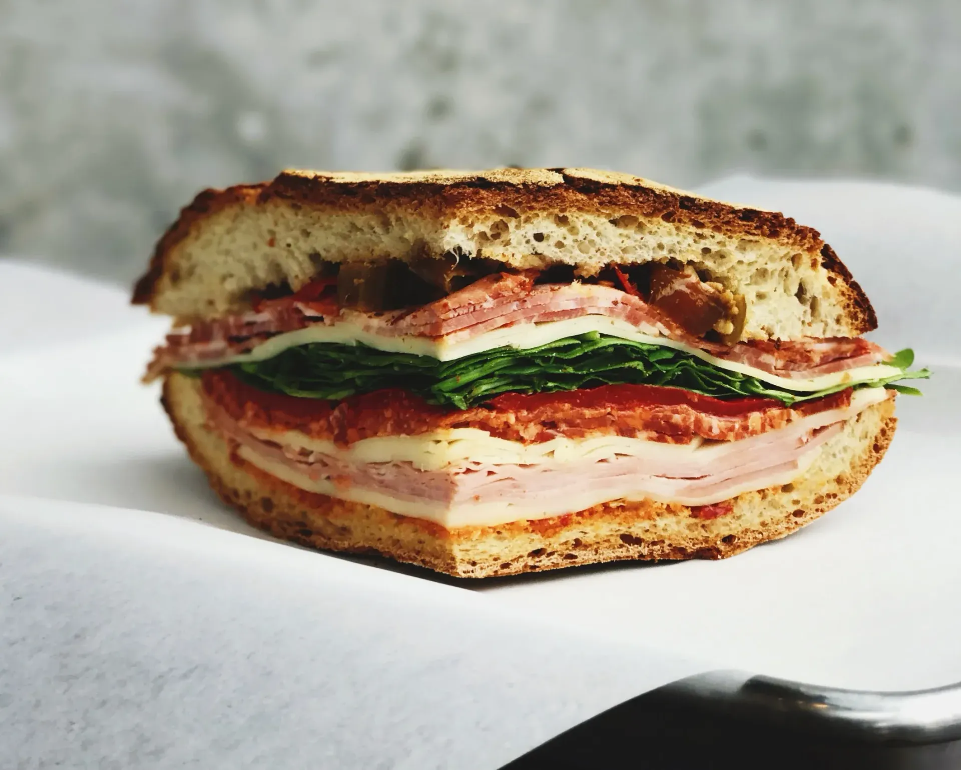 Sandwich cut in half, layers of meat, cheese, lettuce, and tomatoes on bread, on white paper.