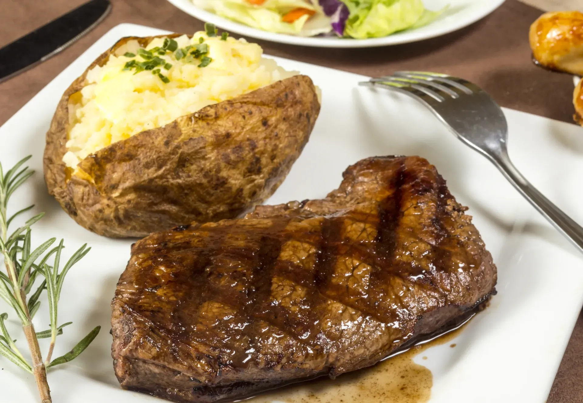 Grilled steak with baked potato on white plate.