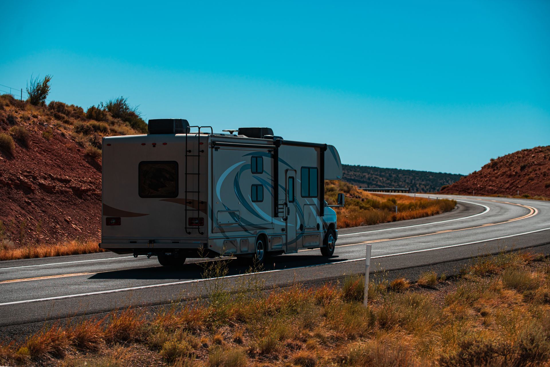 Recreational vehicle driving along a winding desert highway under a clear blue sky. Recreational vehicle driving along a winding desert highway under a clear blue sky.
