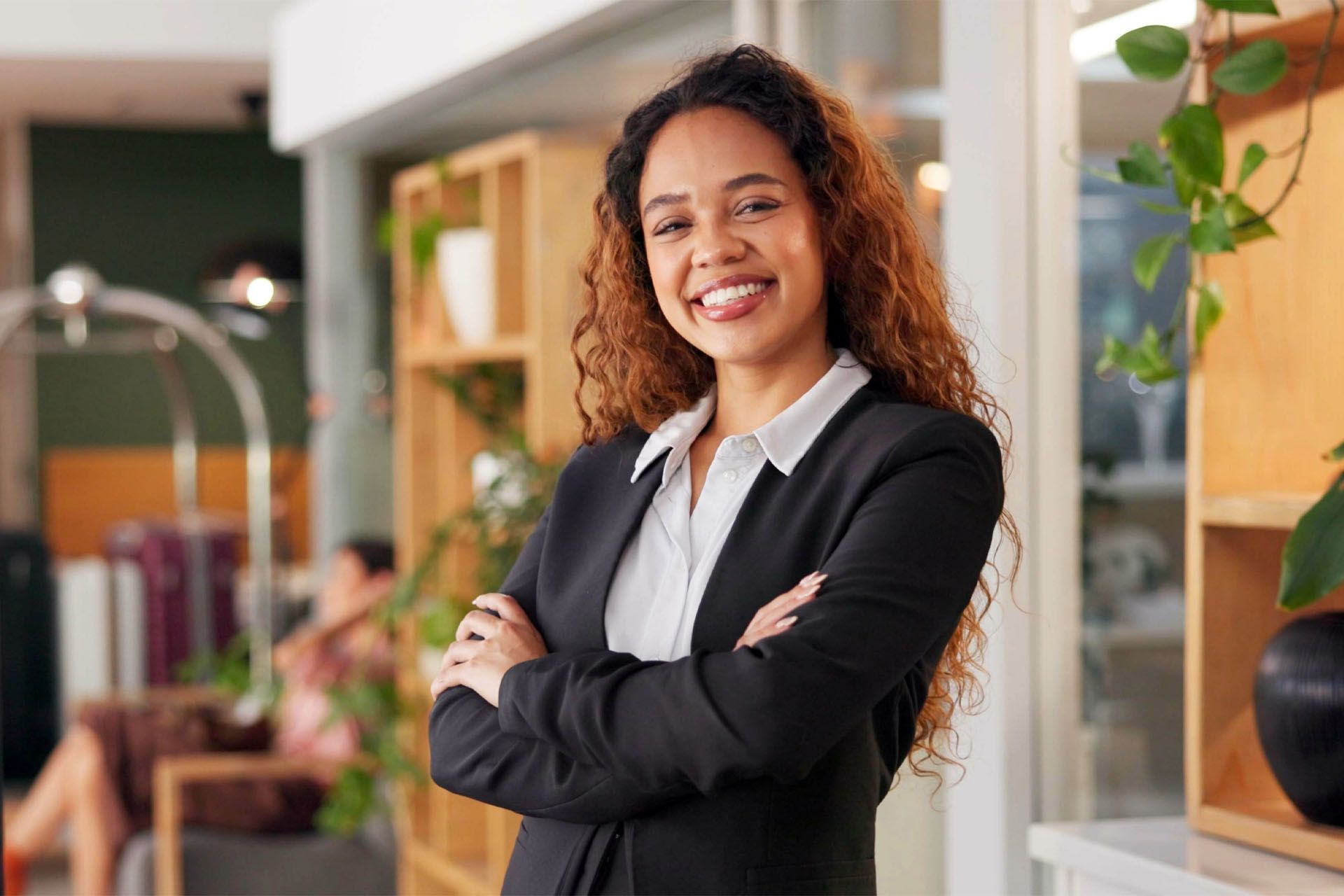 Woman in black blazer with arms crossed, smiling in a well-lit office.