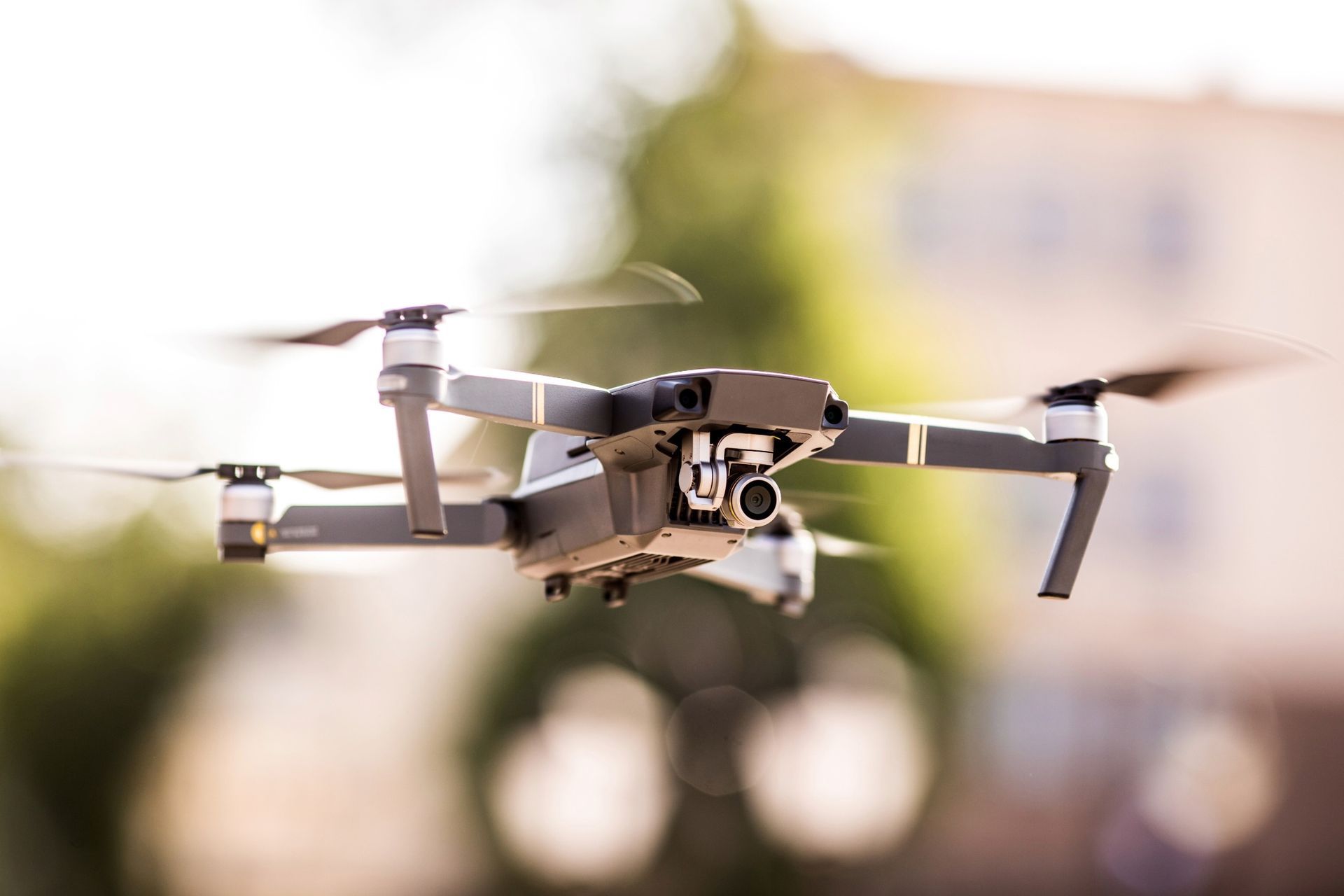 Drone in mid-flight with spinning propellers; blurred background of building and trees.