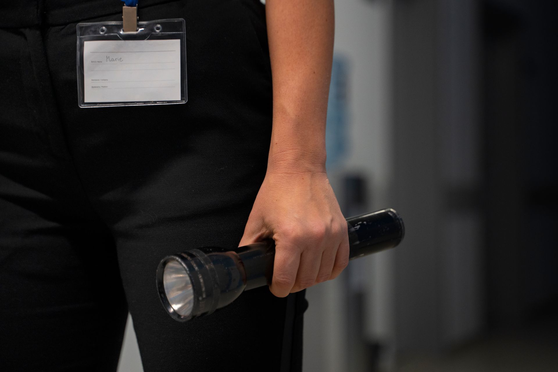 Person in black pants holds a flashlight. A name tag hangs on their shirt.