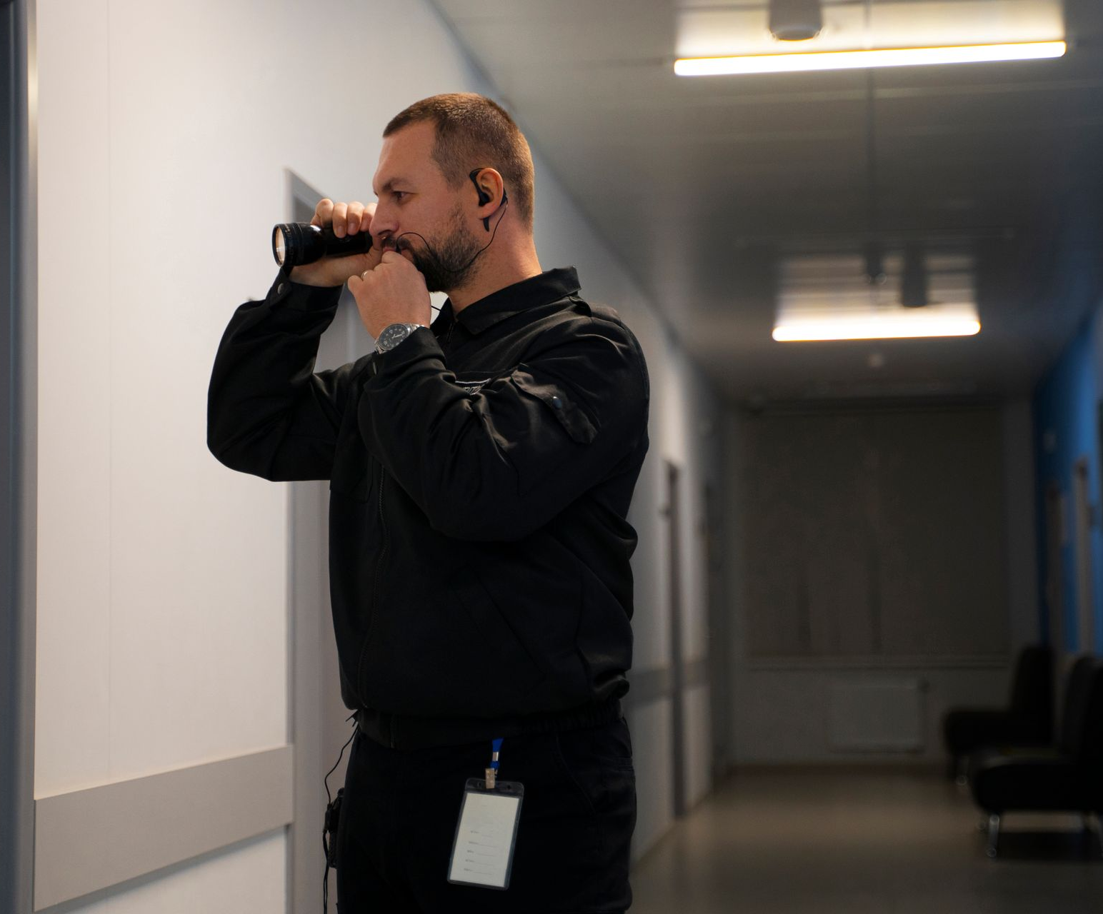 Man in black uniform, using a communication device in a hallway.