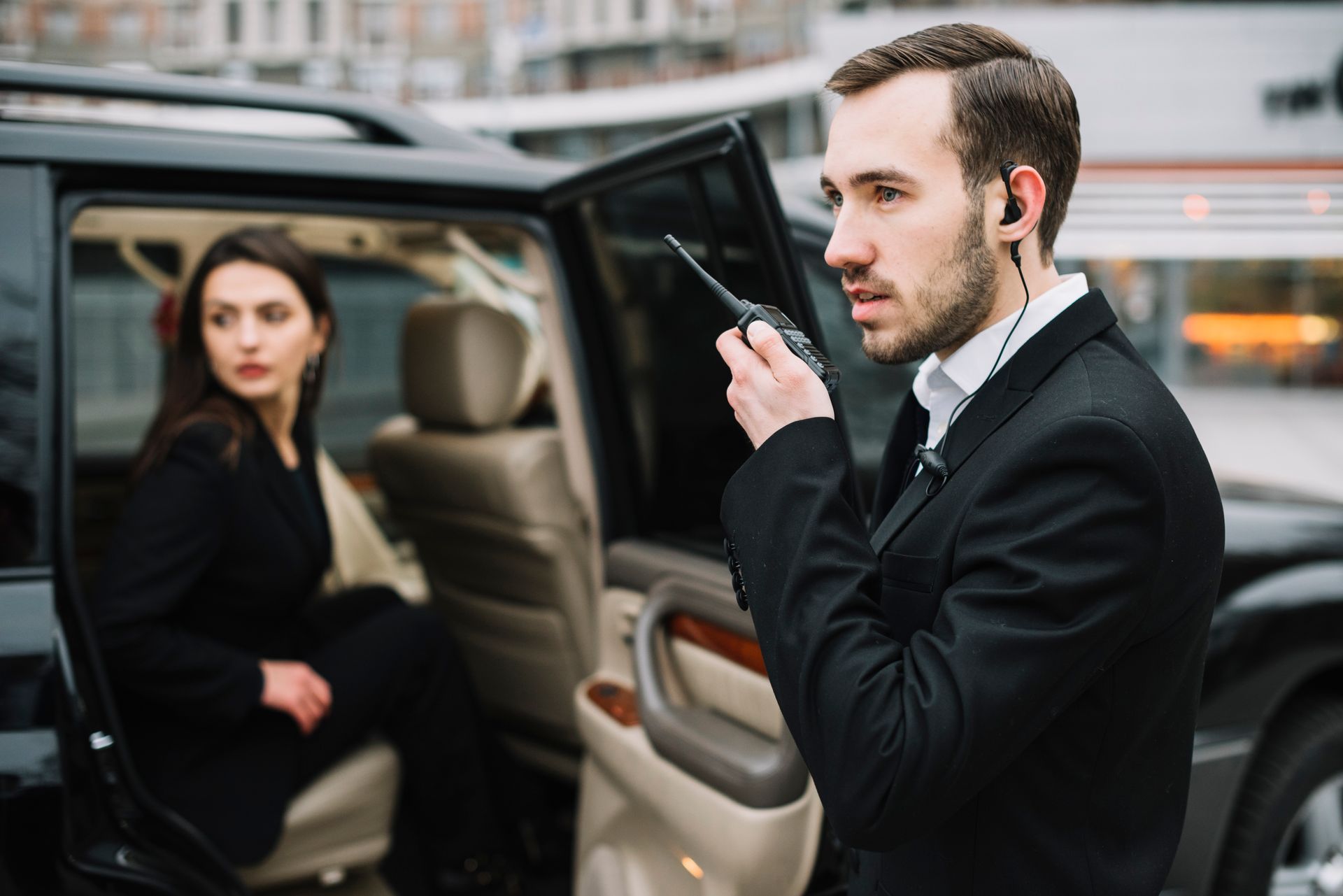Security guard with earpiece and walkie-talkie beside a woman exiting a car.