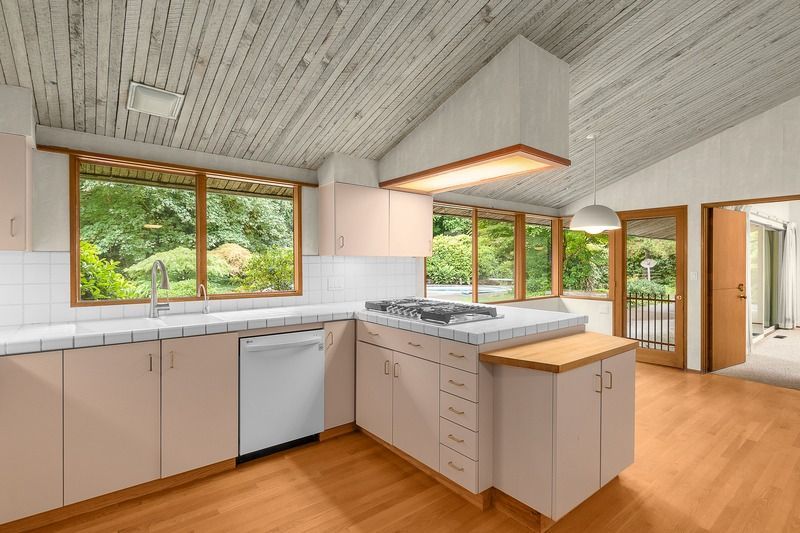 Kitchen with angled, wood-plank ceiling, windows, light-colored cabinets, and an island with a cooktop.