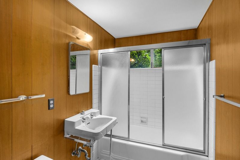 Bathroom with brown wood paneling, a white sink, and a shower with sliding glass doors.