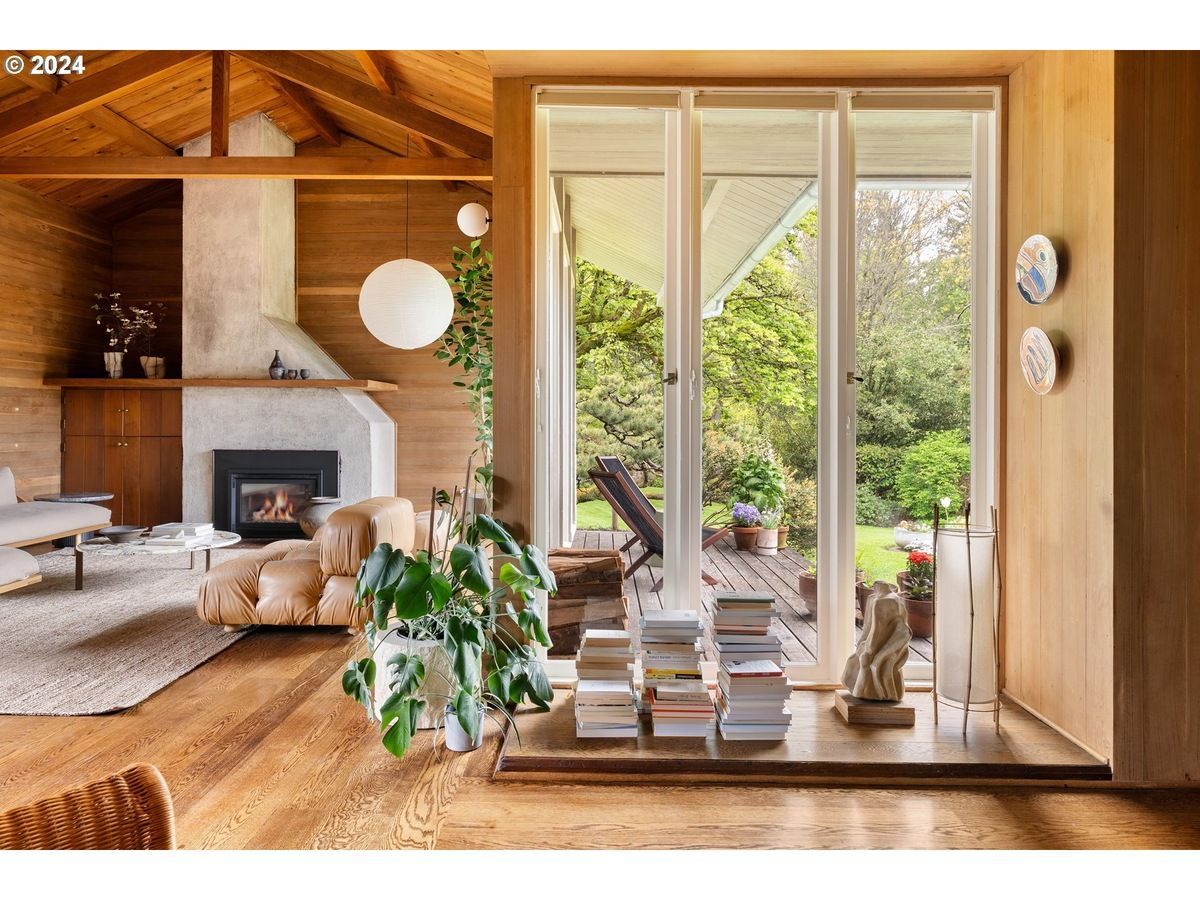 Living room with wood paneling, fireplace, modern furniture, and a view of greenery.