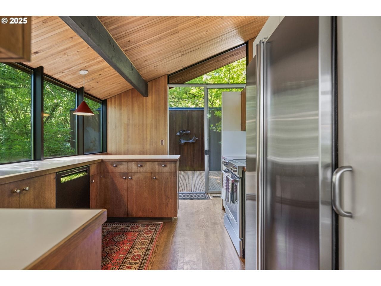 Mid-Century Kitchen with wood ceiling and cabinetry, large windows, stainless steel appliances, and a rug.
