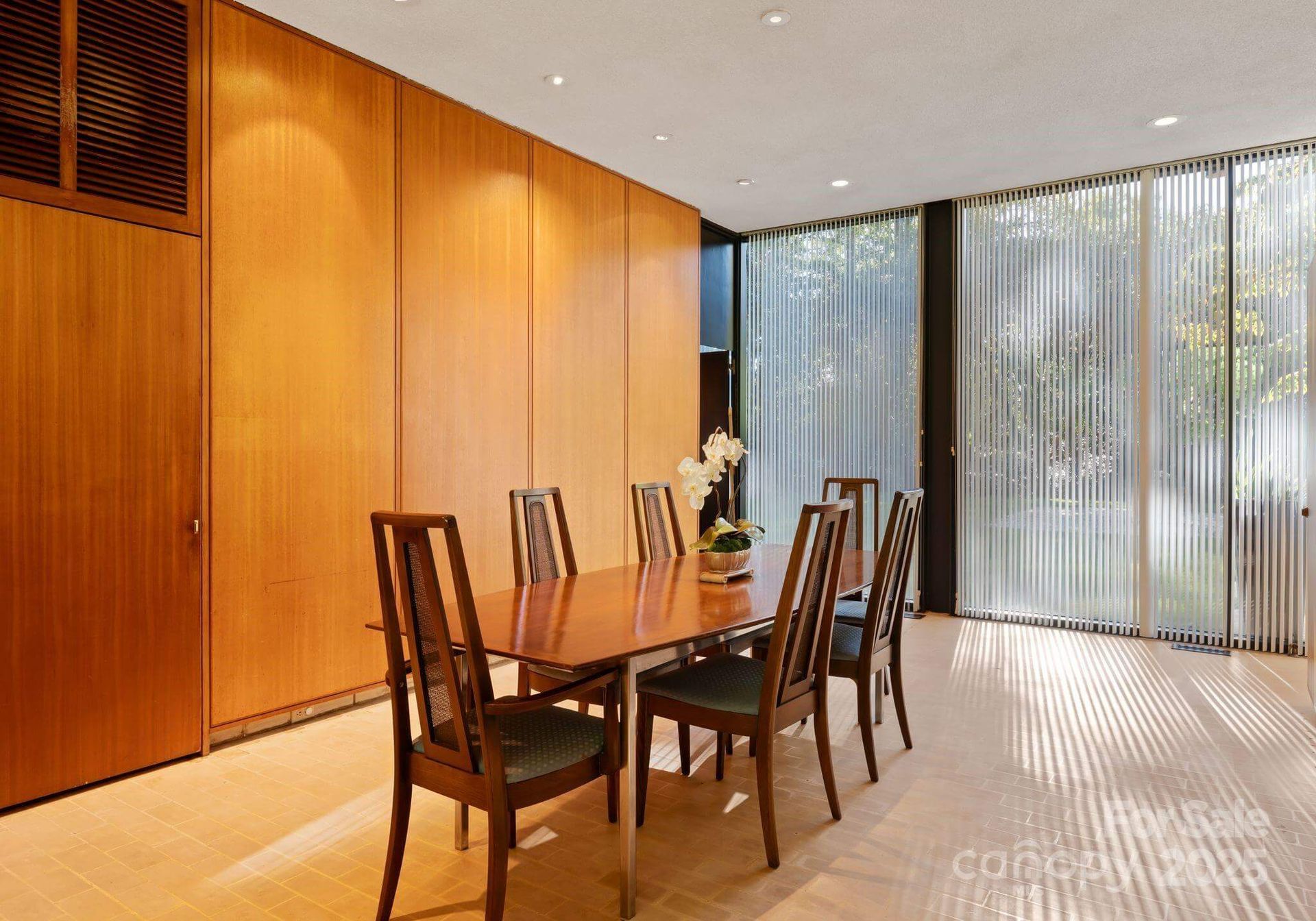 Dining room with wooden paneled walls, a rectangular table, six chairs, and sheer curtains.