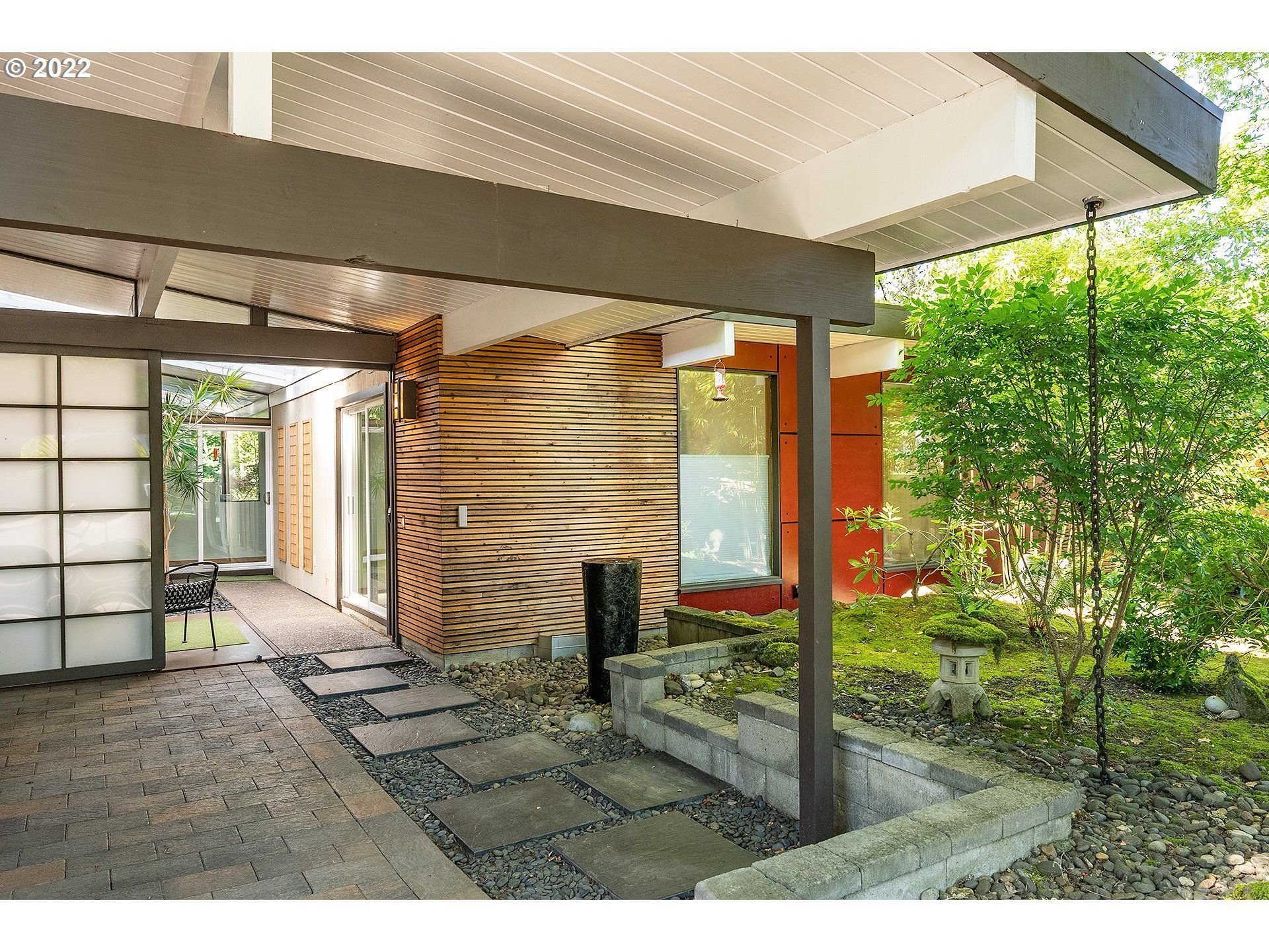 Covered walkway entrance of mid-century modern home with stone path and decorative garden.