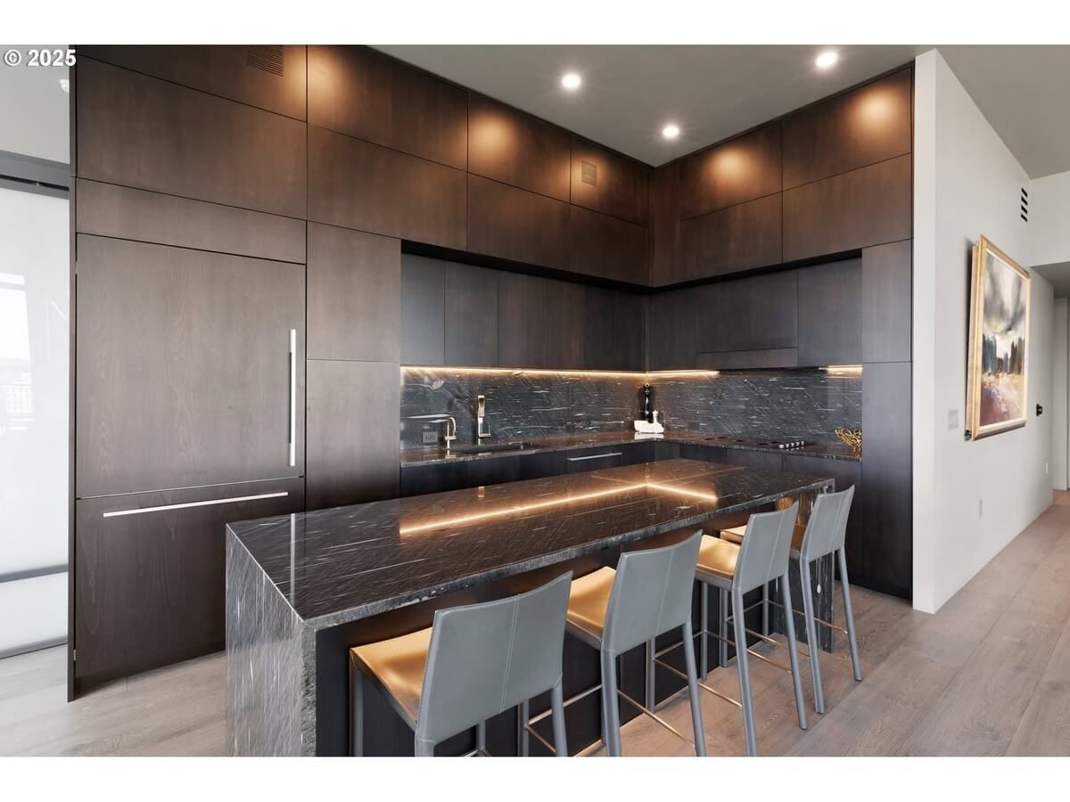 Modern kitchen with dark wood cabinetry, black countertops, and island with stools.