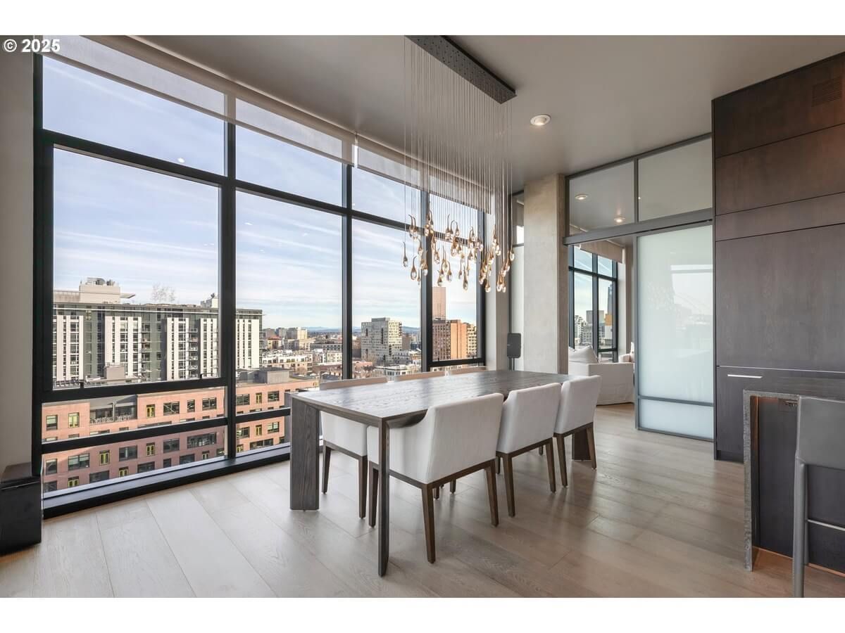 Dining room with large windows overlooking a city, rectangular table with white chairs, modern chandelier.