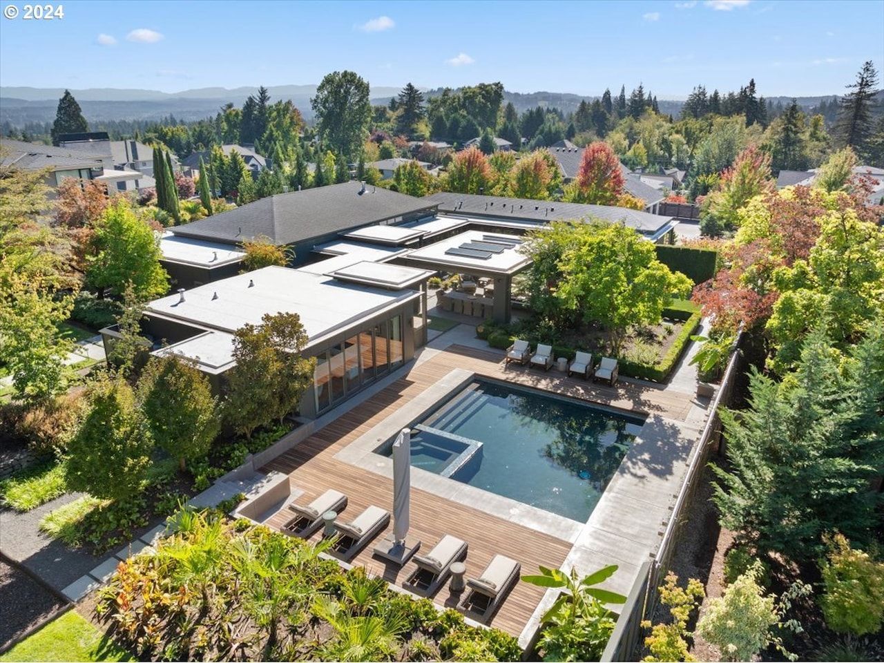 Aerial view of a modern home with a pool and lush landscaping, surrounded by trees.