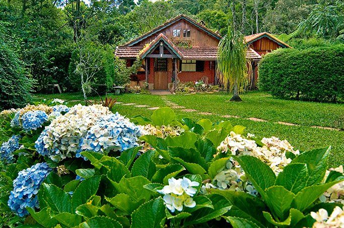 Uma casa no meio de um campo verdejante com flores na frente