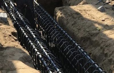 A bunch of black pipes are laying in the dirt.