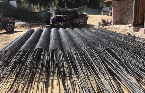 A truck is driving down a dirt road next to a pile of steel bars.