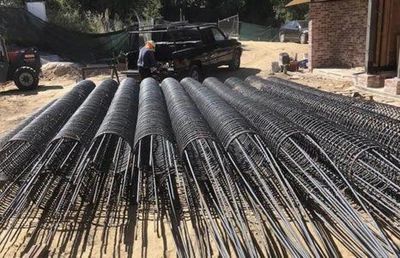 A truck is driving down a dirt road next to a pile of steel bars.