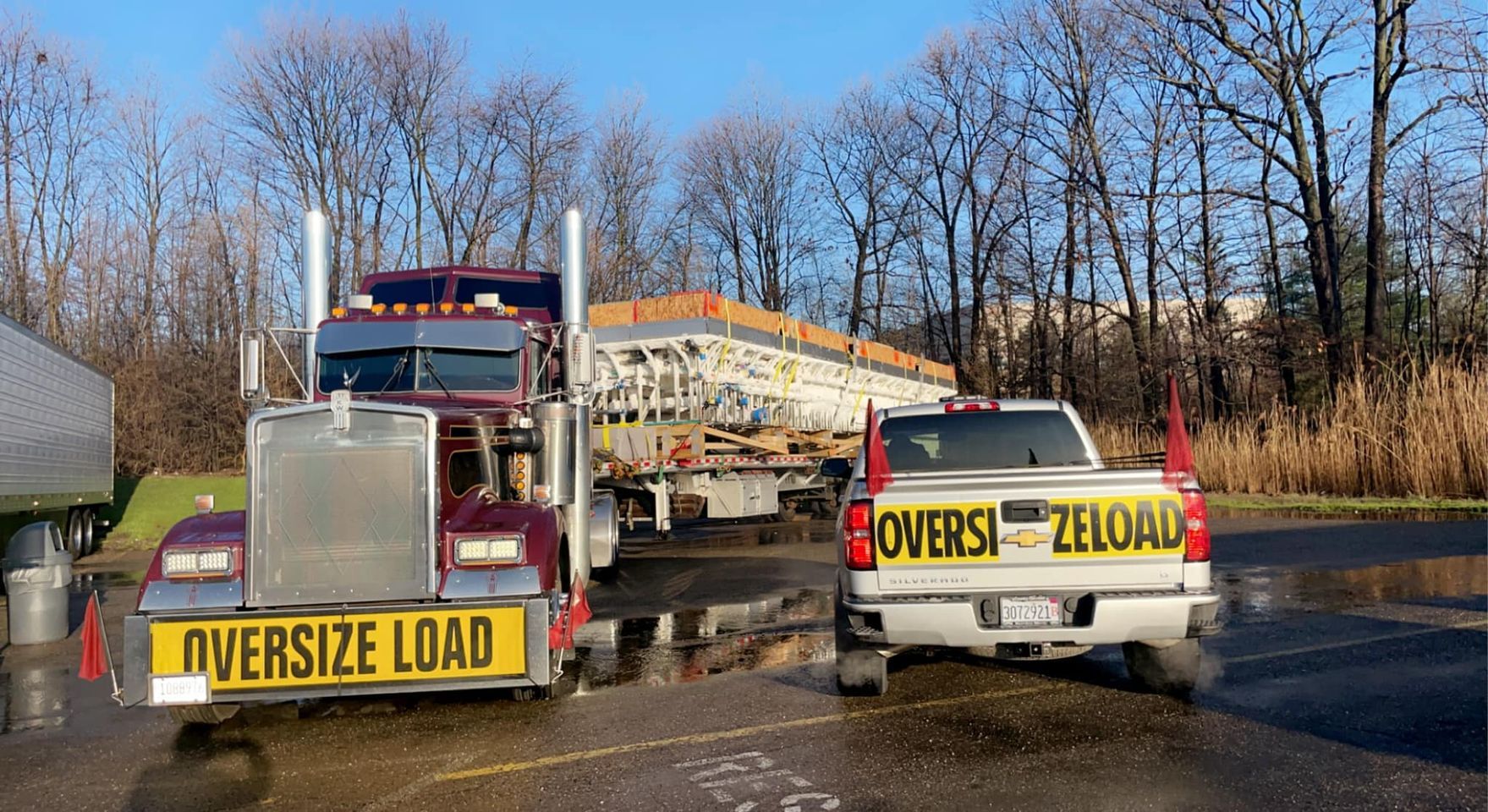 Semi truck hauling oversized load, with escort vehicle in tow; both displaying