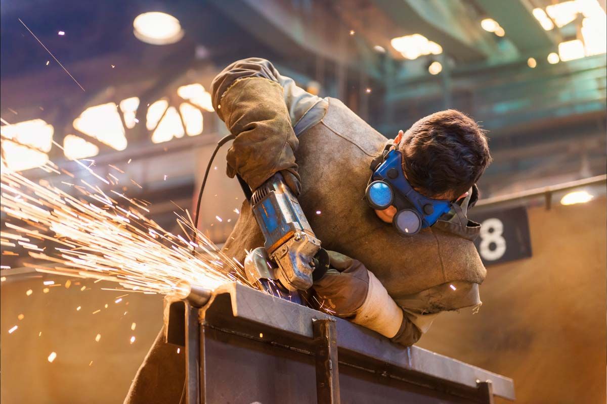Welder in protective gear using a grinder, sparks flying.
