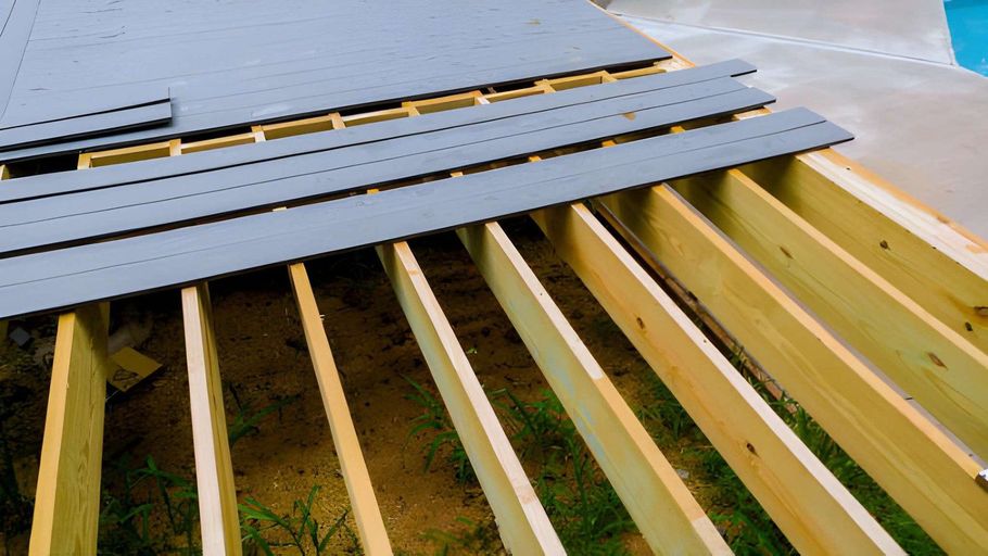 Partially installed gray roof panels on yellow wooden rafters at a construction site
