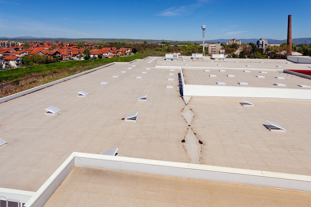 An aerial view of a large, flat commercial roof with multiple skylights and a visible structural crack running down center.