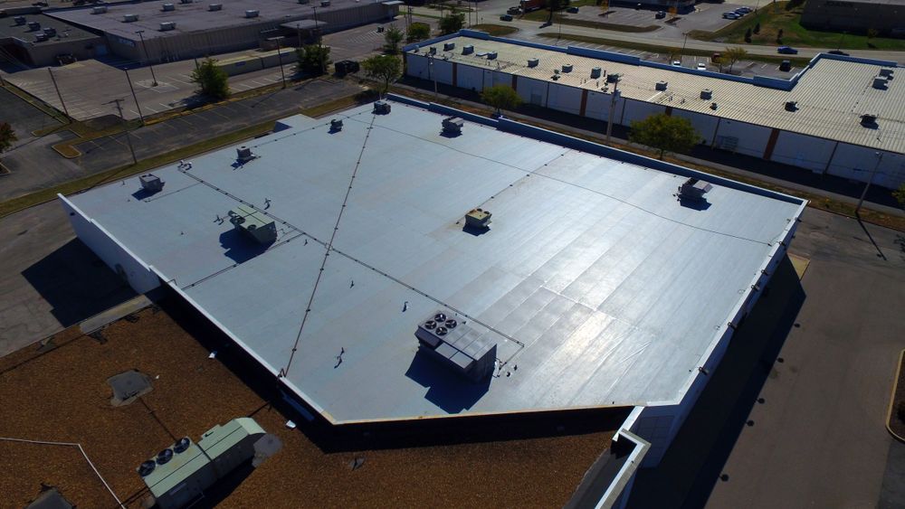 Aerial view of a gray, flat commercial roof with multiple HVAC units and visible seam patterns under bright daylight.