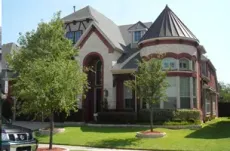 A large, two-story suburban home with stone and brick exterior, a conical turret, and trees on a green front lawn.