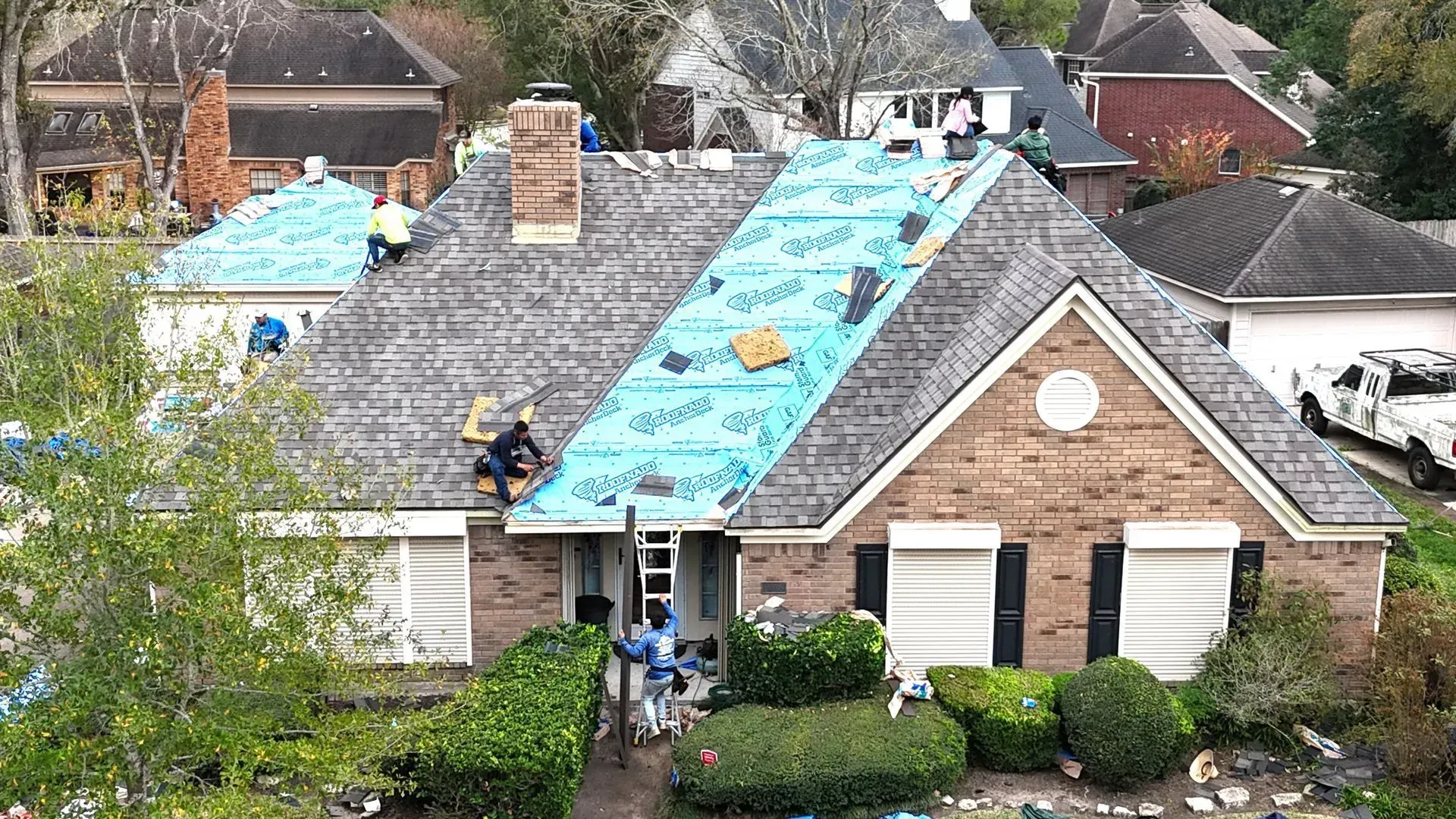 Workers on a residential roof installing blue synthetic underlayment during a roof replacement project.