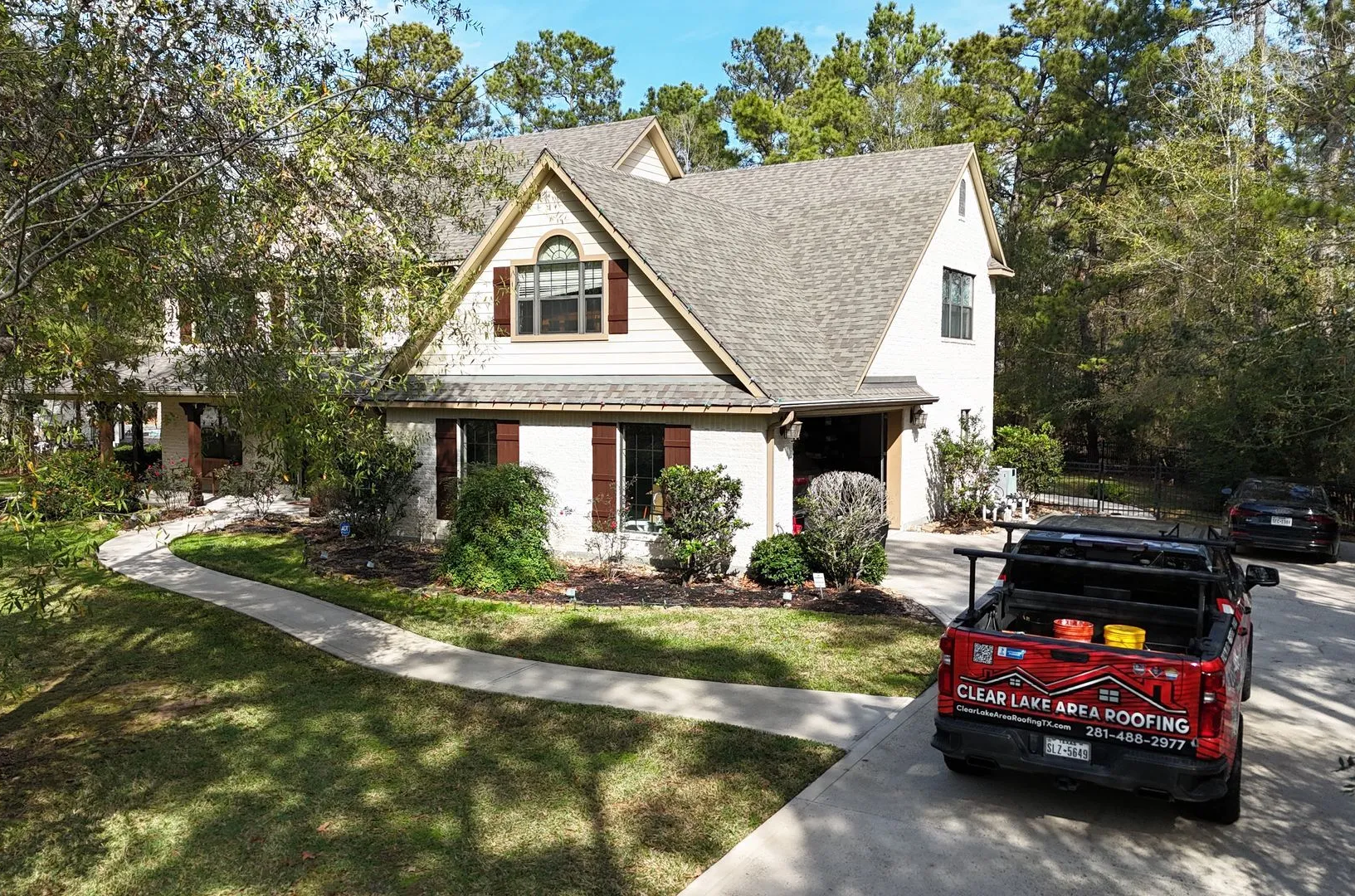 A beige two-story house with a grey roof and brown shutters, seen from a high angle with a red truck in the driveway.