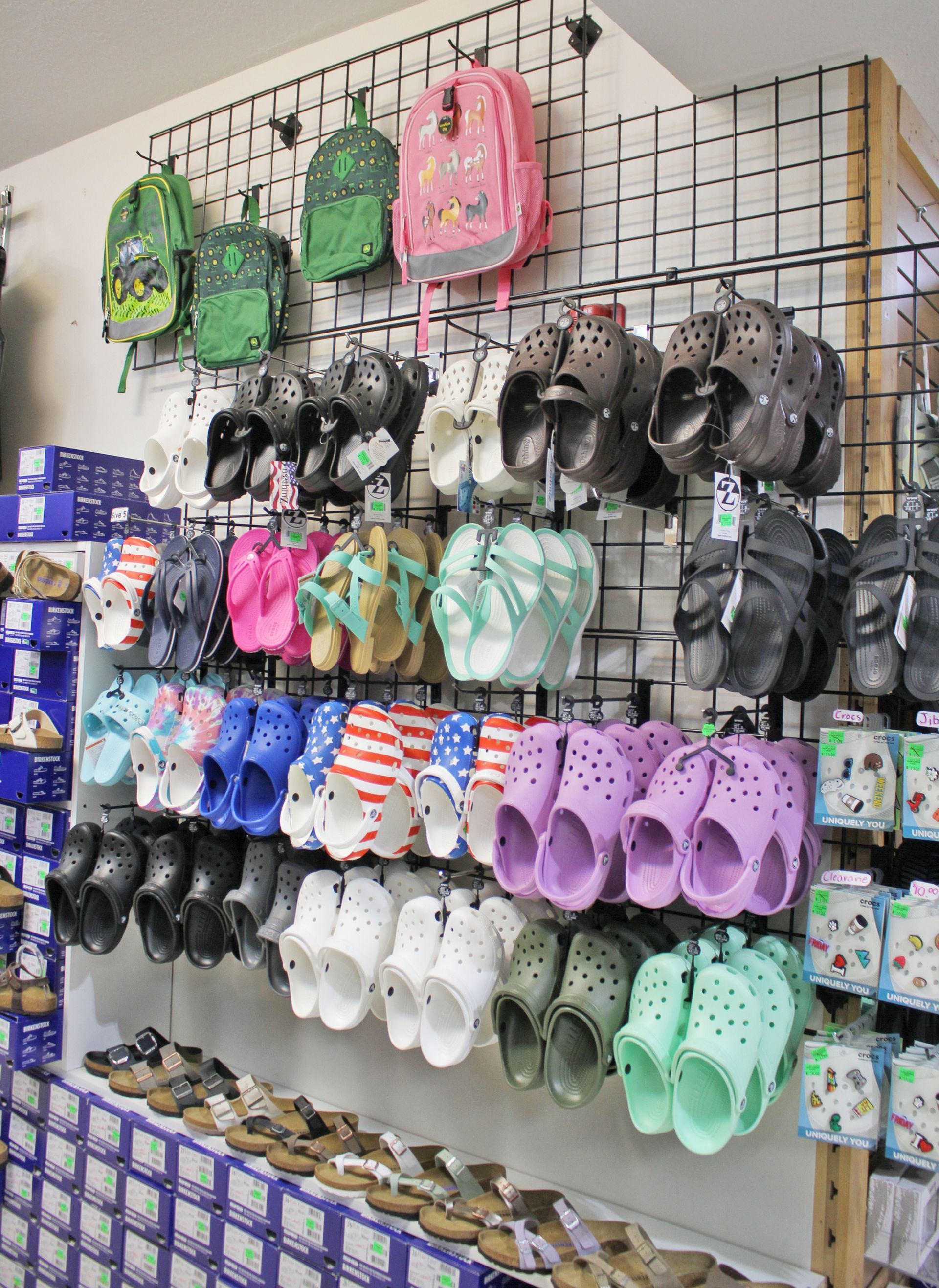 Shoe store display with backpacks, Crocs, and sandals in various colors.