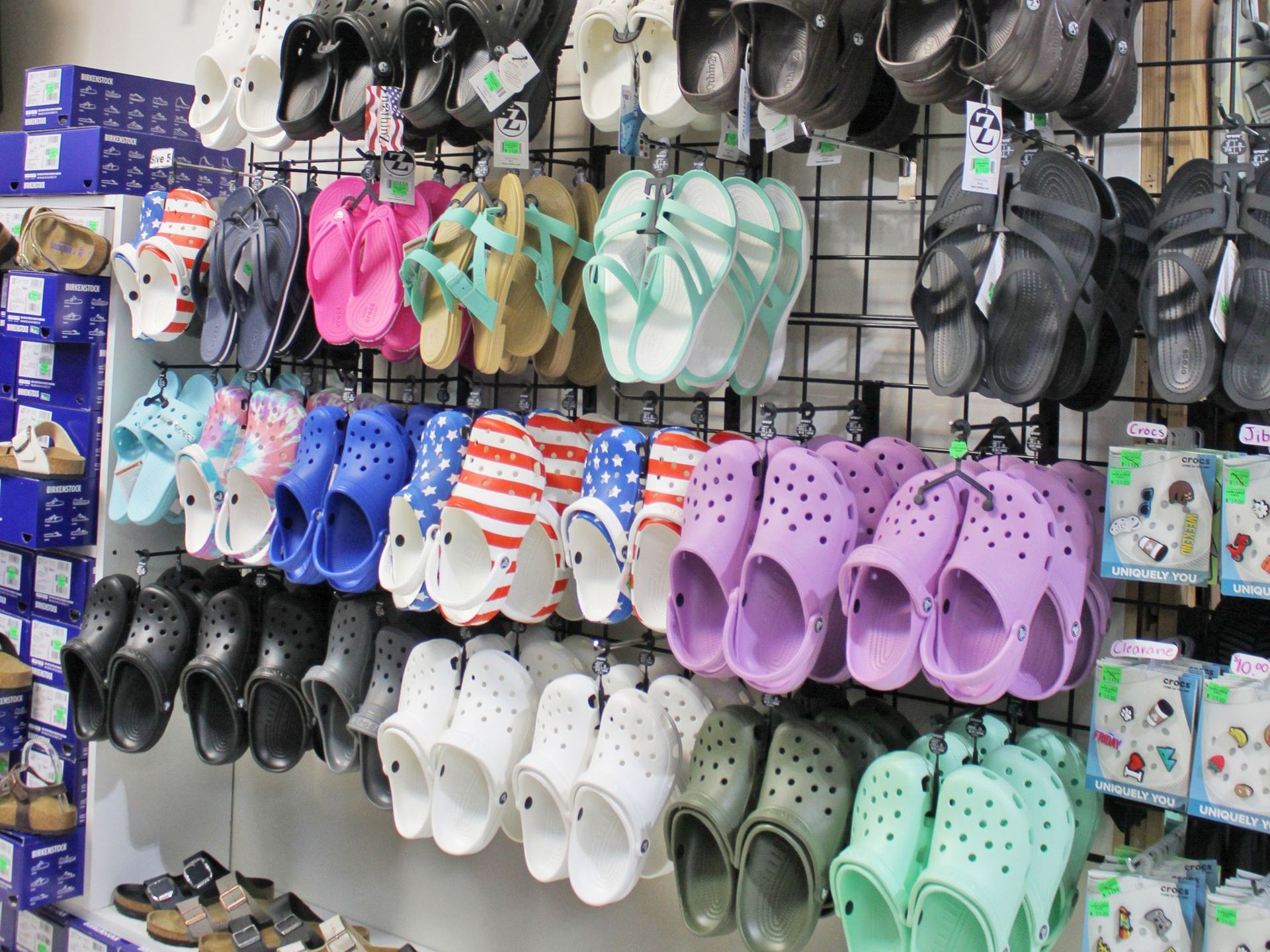 Shoes, including Crocs and sandals, displayed on racks in a store. Variety of colors.