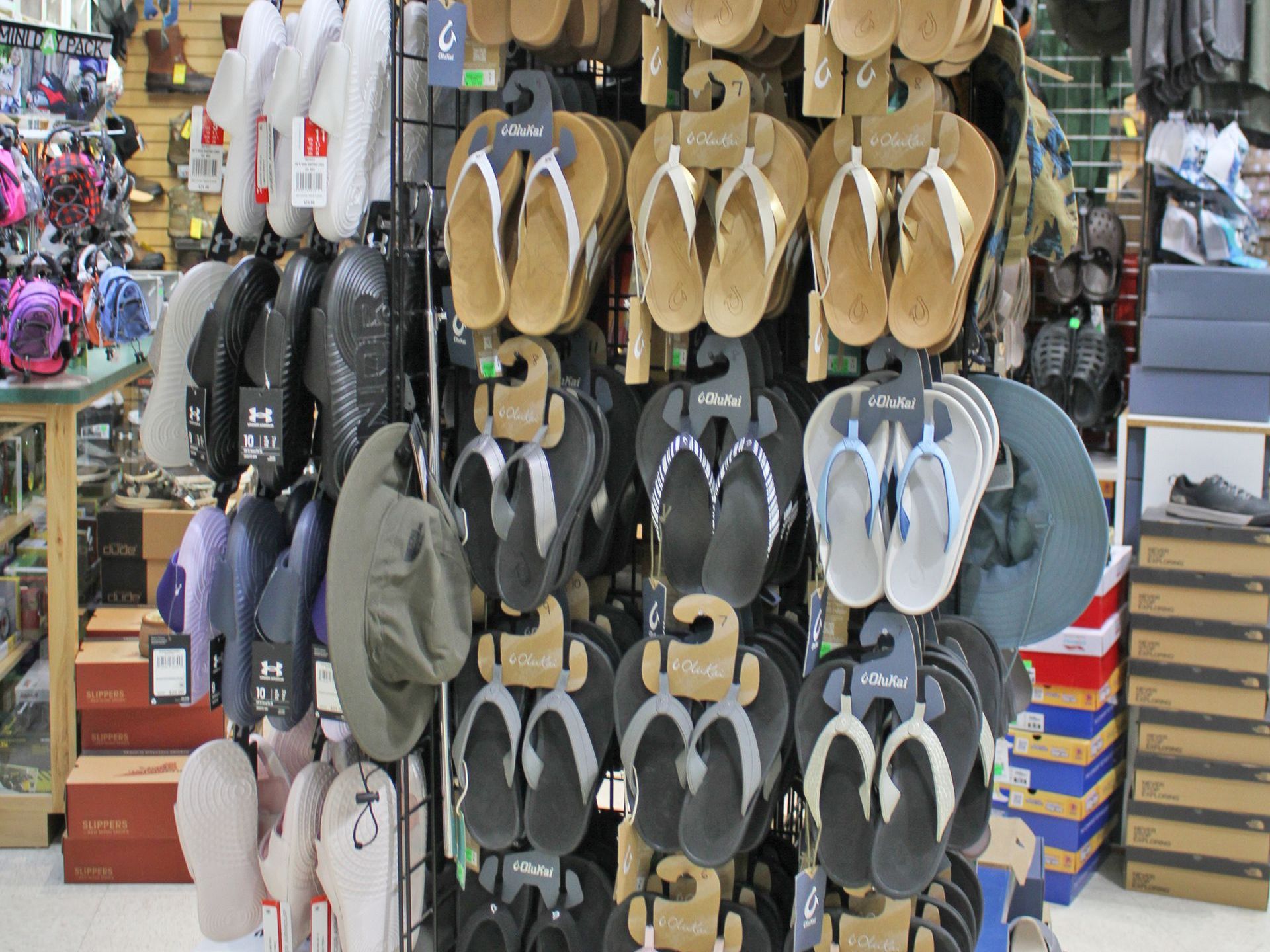 Display of flip-flops and sandals hanging for sale inside a store; various colors.