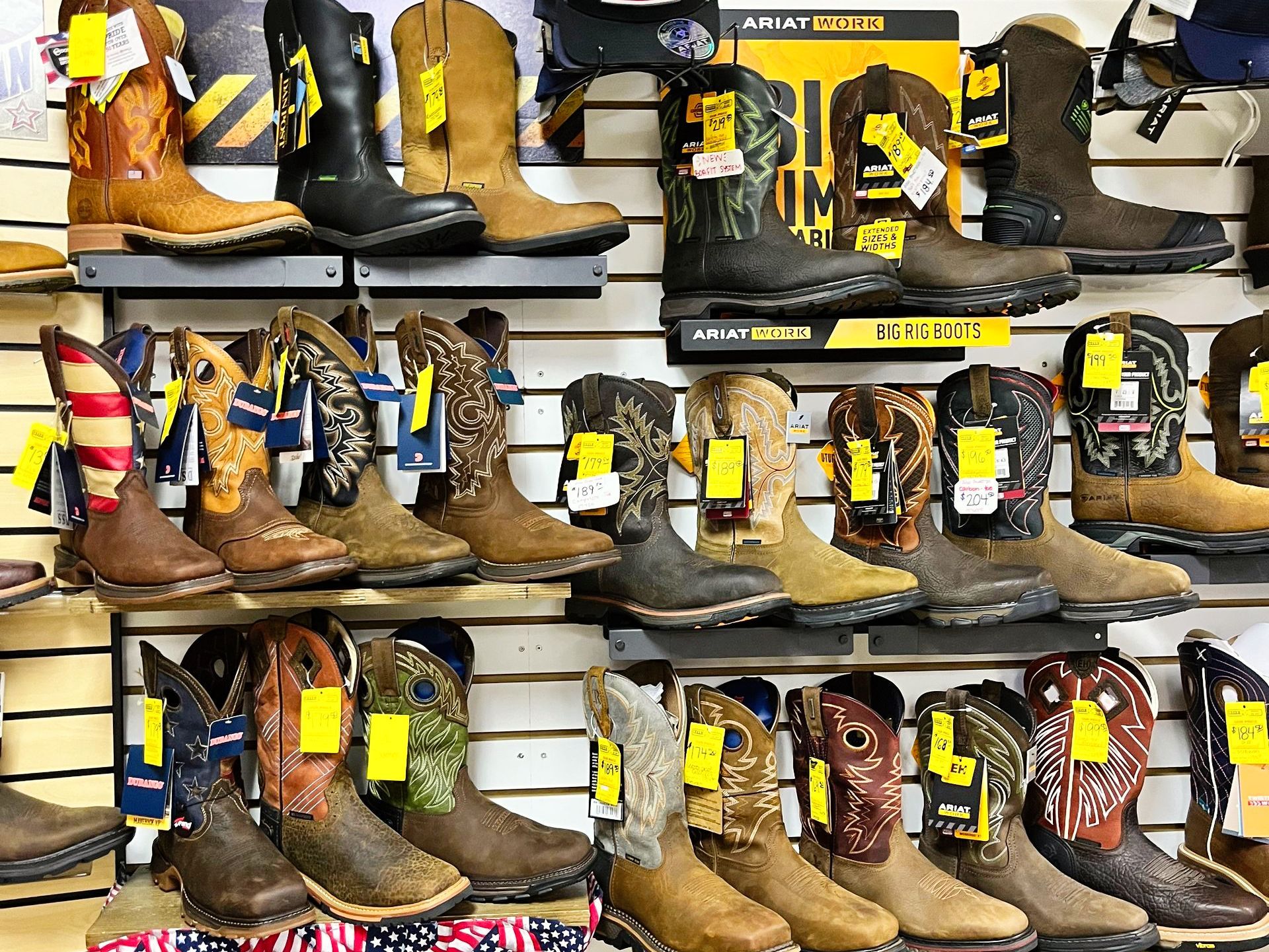 Display of various cowboy boots on shelves in a store, with price tags visible.