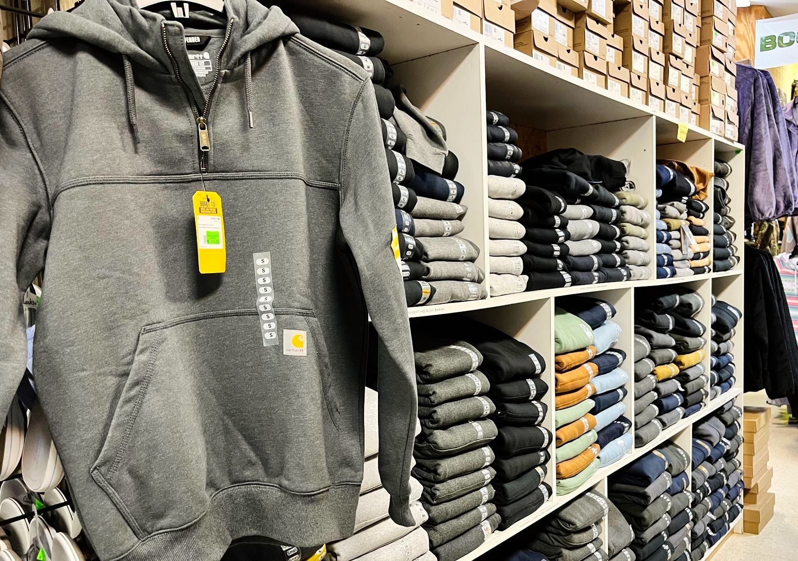 A Carhartt gray hooded sweatshirt displayed near folded clothes on shelves in a store.