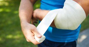 A man in a blue t-shirt, putting a crepe bandage on his arm