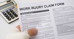 A bandaged hand holding a Work Injury Claim Form
